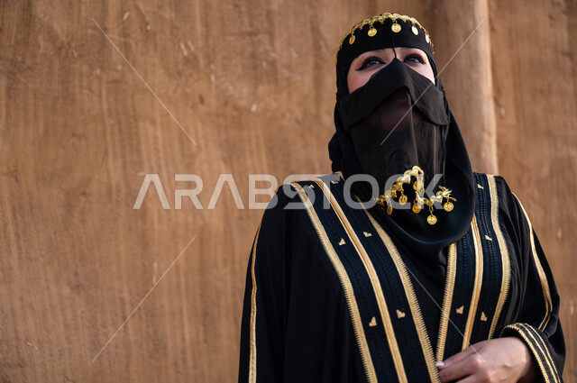 أعياد ومناسبات وطنية سعودية، مفهوم الاهتمام والعناية بالمظهر الخارجي، صورة مقربة لإمرأة خليجية عربية سعودية ترتدي العباءة السوداء والبرقع، يوم التأسيس في 22 فبراير، تأسيس الدولة السعودية الأولى 1727 م، الوقوف بفخر وثقة والنظر الى شيء ما