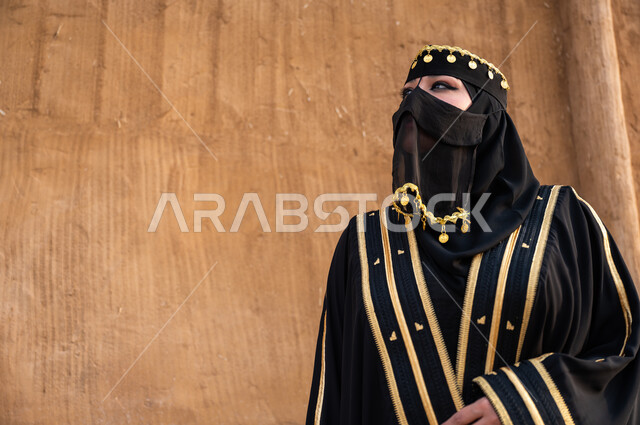 الوقوف بفخر وثقة والنظر الى شيء ما, ارتداء أزياء المنطقة الوسطى في المناسبات الوطنة، مفهوم الاهتمام والعناية بالمظهر الخارجي، صورة مقربة لإمرأة خليجية عربية سعودية ترتدي العباءة السوداء والبرقع، يوم التأسيس في 22 فبراير، تأسيس الدولة السعودية الأولى 1727 م