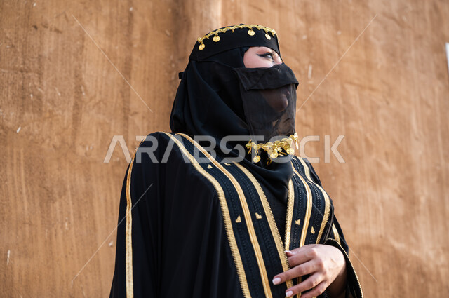 مفهوم الاعتناء بالمظهر الخارجي، ارتداء أزياء المنطقة الوسطى في المناسبات الوطنية، صورة مقربة لإمرأة خليجية عربية سعودية ترتدي العباءة السوداء والبرقع، يوم التأسيس في 22 فبراير، تأسيس الدولة السعودية الأولى 1727 م، الوقوف بفخر وثقة والنظر الى شيء ما