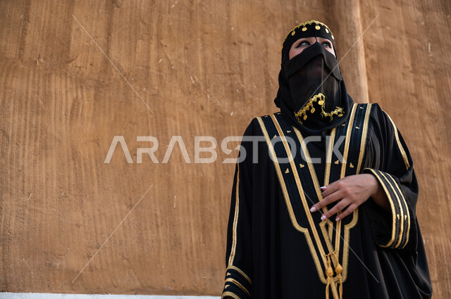 يوم التأسيس في 22 فبراير، ارتداء أزياء المنطقة الوسطى في المناسبات الوطنية، مفهوم الاهتمام والعناية بالمظهر الخارجي، صورة مقربة لإمرأة خليجية عربية سعودية ترتدي العباءة السوداء والبرقع، تأسيس الدولة السعودية الأولى 1727 م، الوقوف بفخر وثقة والنظر الى شيء ما