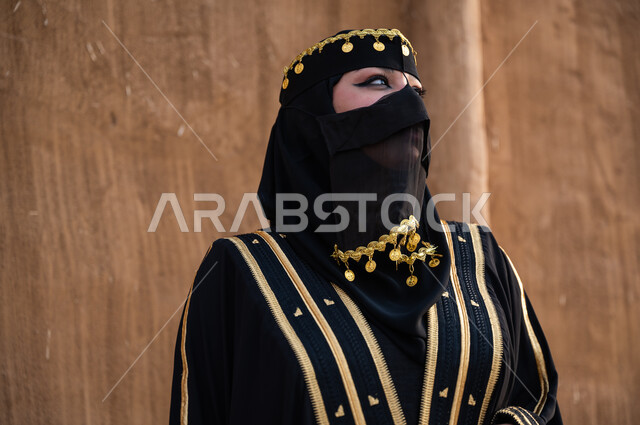 مفهوم الاهتمام والعناية بالمظهر الخارجي، ارتداء أزياء المنطقة الوسطى في المناسبات الوطنية، صورة مقربة لإمرأة خليجية عربية سعودية ترتدي العباءة السوداء والبرقع، يوم التأسيس في 22 فبراير، تأسيس الدولة السعودية الأولى 1727 م، الوقوف بفخر وثقة والنظر الى شيء ما