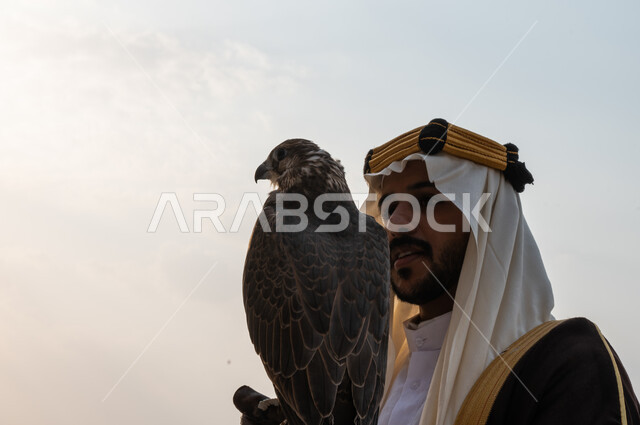 قوة وشجاعة السعوديين في ترويض الطيور الجارحة, فعاليات ترفيهية مع الحيوانات في يوم التأسيس 1727, صورة مقربة من الجانب لرجل عربي خليجي سعودي يرتدي البشت والغترة وقفاز الحماية يحمل طائر الصقر على يده, اكتساب مهارة تدريب الصقور, تأسيس الدولة السعودية الأولى 22 فبراير