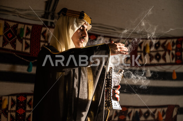 Preparing to celebrate Founding Day 1727 AD, using local aromatic products, establishing the first Saudi state on February 22, using agarwood to perfume with incense, a close-up photo from the side of a Saudi Gulf Arab man wearing a ghutra and bisht, fumigating himself using the incense burner.