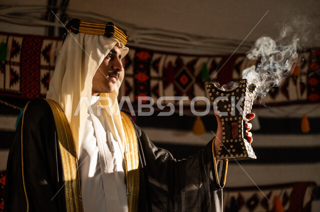 تأسيس الدولة السعودية الأولى 22 فبراير, عراقة وأصالة العادات والتقاليد السعودية, استخدام خشب العود للتطيب بالبخور، ارتداء الأزياء الشعبية في يوم التأسيس 1727, صورة مقربة من الجانب لرجل عربي خليجي سعودي يرتدي الغترة والبشت يقوم بالتعطر باستخدام المبخرة