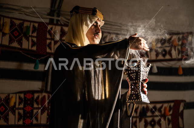 استخدام خشب العود للتطيب بالبخور، ارتداء الأزياء الشعبية في يوم التأسيس 1727, عراقة وأصالة العادات والتقاليد السعودية, صورة مقربة من الجانب لرجل عربي خليجي سعودي يرتدي الغترة والبشت يقوم بالتعطر باستخدام المبخرة, تأسيس الدولة السعودية الأولى 22 فبراير