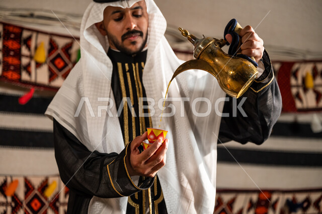 أصالة الخيام الشعبية التراثية, شهامة السعوديين ولهفتهم على إكرام الضيف, صورة مقربة لرجل عربي خليجي سعودي يرتدي الدقلة والغترة ويقوم بتقديم القهوة, اتباع العادات والتقاليد السعودية الأصيلة في حسن الاستقبال , صب القهوة من الدلة النحاسية, منتجات محلية وطنية
