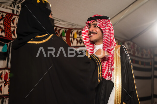 الترابط الأسري والعلاقات الزوجية السعيدة, اهتمام المرأة بمظهر زوجها، زوجة عربية سعودية خليجية ترتدي البرقع والعباءة السوداء تقوم بتعديل لباس الزوج، ارتداء الأزياء الشعبية الوطنية، مفهوم الاهتمام و المودة بين الزوجين