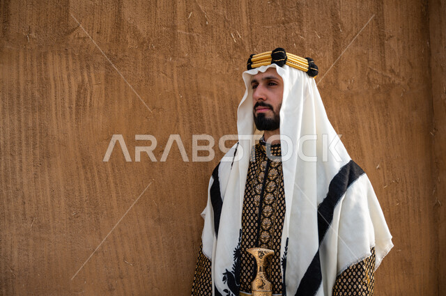 تعزيز الانتماء والولاء للوطن, صورة من الجانب لرجل عربي خليجي سعودي يرتدي الدقلة و الغترة مع المحزم والخنجر يقف بثقة ويقوم بالنظر الى شيء ما, ذكرى يوم التأسيس1727م, ارتداء الجنبية رمز الشجاعة و القوة, تأسيس المملكة 22 فبراير