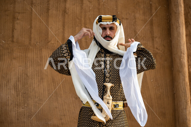 Pride in owning a heritage jabiya, concern for external appearance, anniversary of the founding of the Kingdom in 1727, highlighting the spirit of belonging to the homeland, a close-up photo of a Saudi Gulf Arab man wearing a daqla and a golden aqal and adjusting a ghutra, wearing popular costumes and a belt, Founding Day, February 22