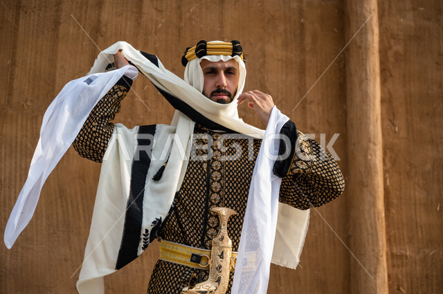 الاهتمام بالمظهر الخارجي, ذكرى تأسيس المملكة 1727, إبراز روح الانتماء للوطن, صورة مقربة لرجل عربي خليجي سعودي يرتدي الدقلة والعقال الذهبي ويقوم بتعديل الغترة, ارتداء الأزياء الشعبية والمحزم,  يوم التأسيس ٢٢ فبراير, الاعتزاز بامتلاك الجنبية التراثية