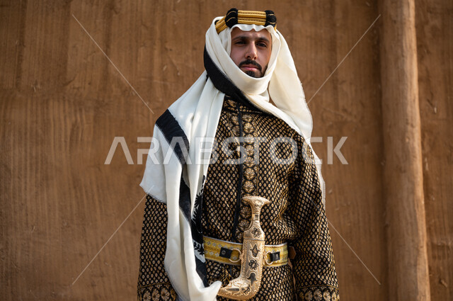 ارتداء الأزياء الشعبية للاحتفال بيوم التأسيس ٢٢ فبراير, مشاعر حب الوطن و الانتماء إليه, صورة مقربة لرجل عربي خليجي سعودي يرتدي الدقلة و الغترة مع المحزم والخنجر يقف بثقة ويقوم بالنظر الى شيء ما, تأسيس الدولة السعودية الأولى 1727 , الاعتزاز بامتلاك الجنبية التراثية