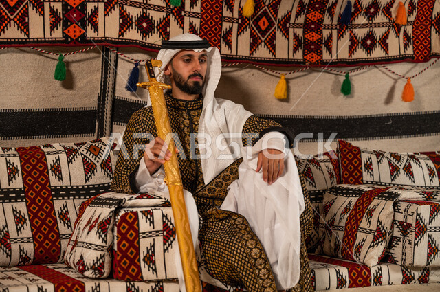 التباهي بالأسلحة التقليدية السعودية, حب وشغف امتلاك السيوف التراثية, الجلوس داخل خيمة شعبية بإيماءات الاعتزاز والفخر, رجل عربي خليجي سعودي يرتدي الدقلة والغترة و يحمل السيف الى جانبه, توارث العادات و التقاليد الأصيلة