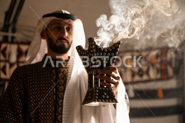 أصالة العادات والتقاليد السعودية, روائح عطرية محببة لدى أبناء الخليج, صورة مقربة لرجل عربي خليجي سعودي يرتدي الغترة والدقلة يقوم بالتبخر والتطيب بالبخور باستخدام المبخرة, استخدام خشب العود في المناسبات السعودية