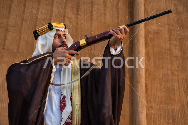 The prowess of the Saudis in hunting, the establishment of a falconry club in the Kingdom on the anniversary of the founding of the first state in 1727, the use of a rifle to hunt wild animals, a close-up photo of a Saudi Gulf Arab youth wearing a ghutra and a bisht and hunting birds of prey, appointment and focus on the target, Founding Day, February 22