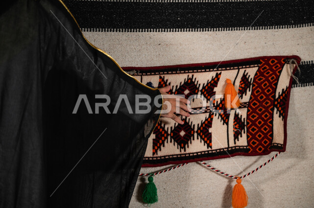 الفخر والتباهي بالمجالس العربية، التطريز بالنقوش الشعبية التقليدية العريقة، صورة مقربة ليد رجل عربي خليجي سعودي يقوم بلمس جدار الخيمة القماشي، قماش الخيام المصنوع من شعر الماعز ، الاعتزاز بالتراث الشعبي السعودي