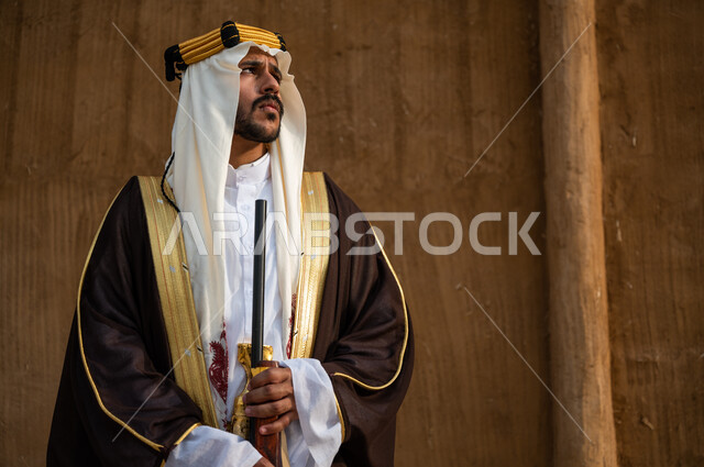 ذكرى تأسيس المملكة 1727, ارتداء الأزياء الشعبية الوطنية, إحياء تاريخ الأجداد والاحتفال بإنجازاتهم, اهتمام أبناء المملكة بهواية صيد الصقور، صورة مقربة لرجل عربي خليجي سعودي يرتدي البشت والغترة يحمل البندقية بفخر وينظر الى شيء ما، الاحتفال بيوم التأسيس 22 فبراير