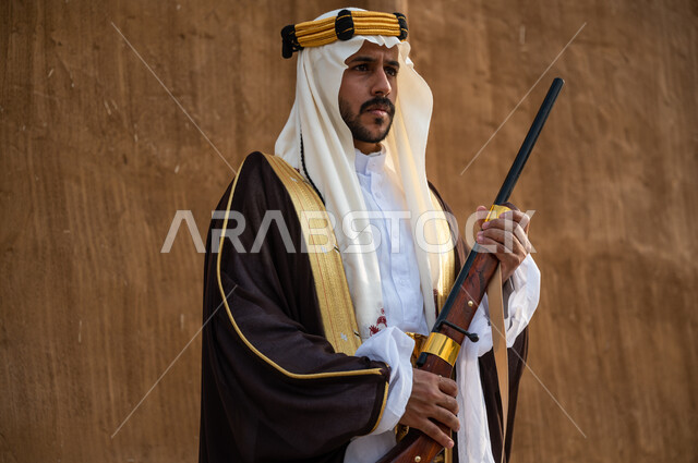 ارتداء الأزياء الشعبية الوطنية, إحياء تاريخ الأجداد والاحتفال بإنجازاتهم, اهتمام أبناء المملكة بهواية صيد الصقور، صورة مقربة لرجل عربي خليجي سعودي يرتدي البشت والغترة يحمل البندقية بفخر وينظر الى شيء ما، الاحتفال بيوم التأسيس 22 فبراير، ذكرى تأسيس المملكة 1727