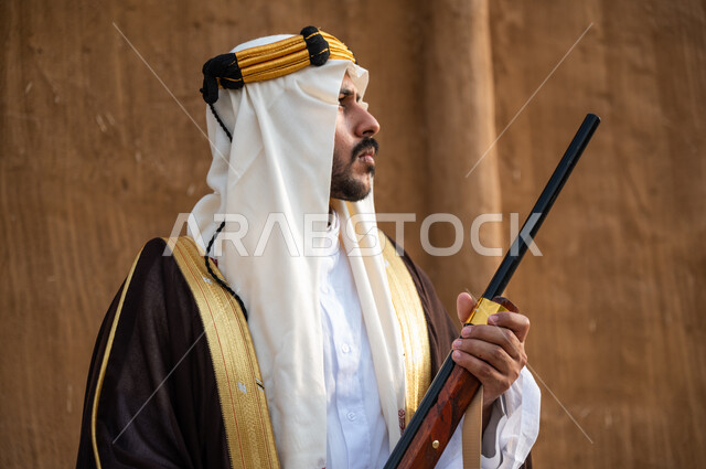 ذكرى تأسيس الدولة السعودية الأولى 1727م، توارث مهنة صيد الصقور بين أبناء الوطن، استخدام البندقيه لصيد الطيور والحيوانات البرية، صورة مقربة لرجل عربي خليجي سعودي يرتدي البشت والغترة الشعبية في الاعياد الوطنية ، التأمل و النظر إلى شيء ما، يوم التأسيس 22 فبراير