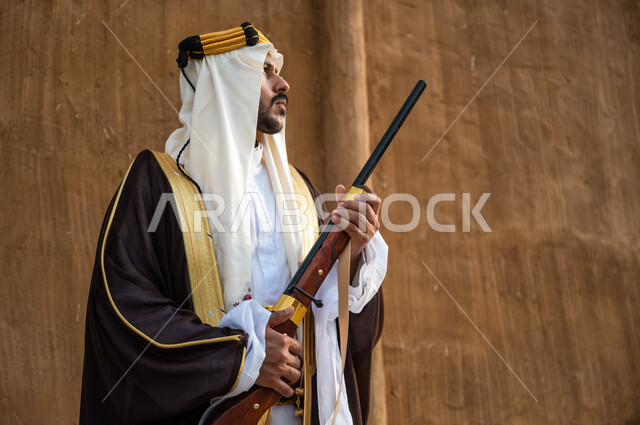 توارث مهنة صيد الصقور بين أبناء الوطن، استخدام البندقيه لصيد الطيور والحيوانات البرية، صورة مقربة لرجل عربي خليجي سعودي يرتدي البشت والغترة الشعبية في الاعياد الوطنية ، ذكرى تأسيس الدولة السعودية الاولى 1727م، التأمل و النظر إلى شيء ما، يوم التأسيس 22 فبراير