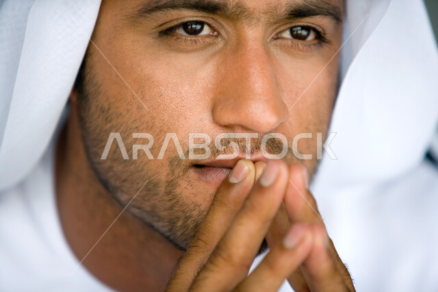 نظرات مليئة بالذكاء والفطنة   ، بورتريه مقرب لرجل عربي  خليجي إماراتي  يرتدي الزي الإماراتي التقليدي وينظر إلى الأمام  , إيماءات وجه تدل على التفكير بتمعن والتخطيط والتأمل ، خلفية رمادية .