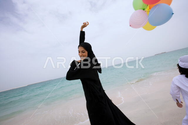 الشعور بالسعادة في قضاء إجازة الصيف  ,  أم عربية إماراتية خليجية ترتدي العباءة السوداء وتقوم  باللعب مع ولدها بالبالونات على شاطئ البحر ،الإستمتاع  بالفعاليات الصيفية العائلية ،  السياحة في دول الخليج العربي ، منتجعات شاطئية في الإمارات . 
