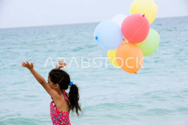 الترفيه والتسلية بقضاء أوقات صيفية ممتعة ,  فتاة عربية إماراتية خليجية ترتدي زي البحر وتقوم باللعب بالبالونات على شاطئ البحر ،الإستمتاع  بفعاليات إجازة الصيف ،  السياحة في دول الخليج العربي ، منتجعات شاطئية في الإمارات .