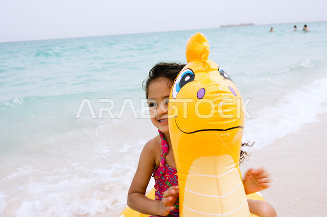 قضاء أوقات صيفية ممتعة بالترفيه والتسلية  ,  فتاة عربية إماراتية خليجية ترتدي زي البحر وتقوم باللعب بالألعاب الهوائية المطاطية على شاطئ البحر ،الإستمتاع  بفعاليات إجازة الصيف ،  السياحة في دول الخليج العربي ، منتجعات شاطئية في الإمارات .