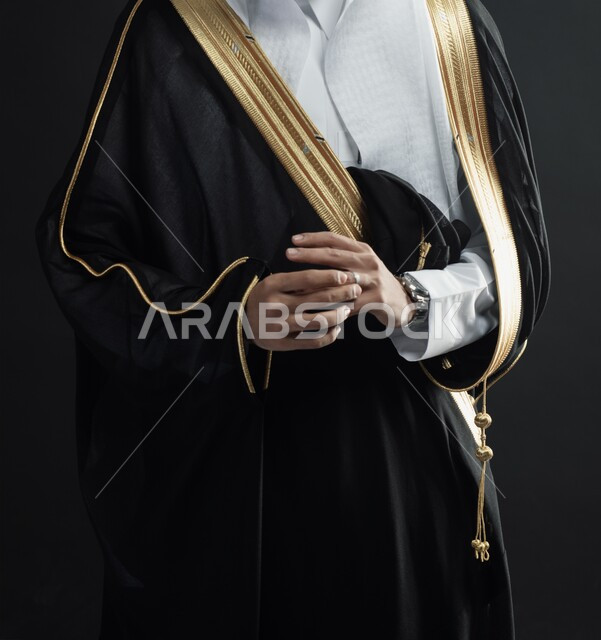 الاهتمام بالاناقة والمظهر الخارجي، المناسبات والأفراح السعودية، بورتريه مقرب لعريس عربي خليجي سعودي بالبشت الأسود ويرتدي بيده ساعة يد وخاتم الزواج، رجل سعودي بالزي الرسمي في يوم زفافه، خلفية سوداء