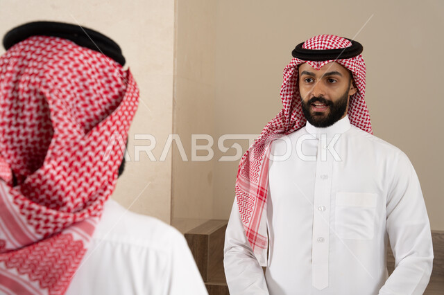 Reservation and entry procedures at the reception desk, customer service in tourist hotels, a Saudi Gulf Arab young man wearing a thobe and shemagh working in the information field, wearing traditional Saudi dress, inquiring and inquiring about hotel services