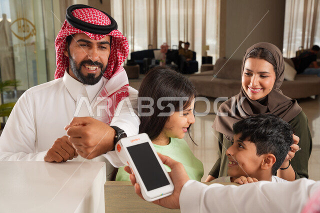 استخدام الوسائل والتقنيات الحديثة في الدفع الالكتروني, عائلة عربية خليجية سعودية في إحدى الفنادق الفاخرة, سهولة الدفع الالي في السعودية, التحكم بالحجوزات والدفع من خلال ساعة السمارت عبر الجوال, الاستمتاع بقضاء وقت ممتع مع الأسرة بإيماءات السعادة والسرور