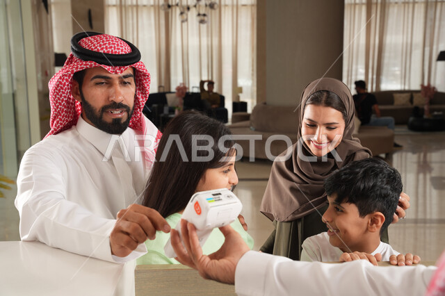 سهولة الدفع الالي في السعودية, استخدام الوسائل والتقنيات الحديثة في الدفع الالكتروني, عائلة عربية خليجية سعودية في إحدى الفنادق الفاخرة, تأكيد الحجز الفندقي لموظف الاستقبال عبر الانترنت, الاستمتاع بقضاء وقت ممتع مع الأسرة بإيماءات السعادة والسرور