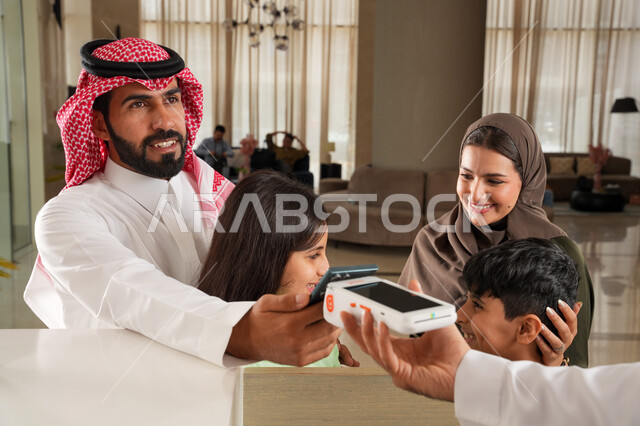 تأكيد الحجز الفندقي لموظف الاستقبال عبر الانترنت, استخدام الوسائل والتقنيات الحديثة في الدفع الالكتروني, عائلة عربية خليجية سعودية في إحدى الفنادق الفاخرة, سهولة الدفع الالي في السعودية, الاستمتاع بقضاء وقت ممتع مع الأسرة بإيماءات السعادة والسرور