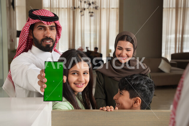 الحجوزات الالكترونية للفنادق وتذاكر السفر عبر الهاتف المحمول, تأكيد الحجز الفندقي لموظف الاستقبال عبر الجوال, عائلة عربية سعودية خليجية في إحدى الفنادق الفاخرة, عرض شاشة خضراء فارغة, كروما, ايماءات السعادة والسرور