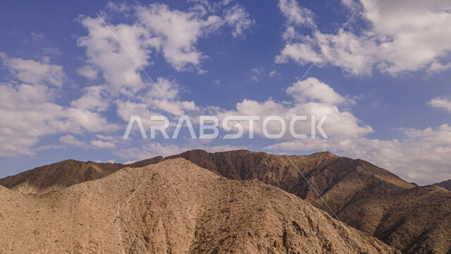 الغيوم والسحب البيضاء في السماء وقت النهار، القمم والمرتفعات الجبلية في ولاية بوشر في محافظة مسقط، منحدرات الجبال الصخرية الطبيعية في سلطنة عمان، معالم ولاية بوشر المشهورة