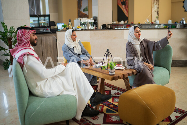 جلسات وناسة وتعارف, التقاط صور سيلفي تذكارية عبر الجوال برفقة زملاء العمل, مجموعة أصدقاء عرب خليجيون سعوديون في إحدى المقاهي الراقية في المملكة, النظر إلى الكاميرا بإيماءات السرور والسعادة, توثيق اللحظات وبناء علاقات اجتماعية ناجحة