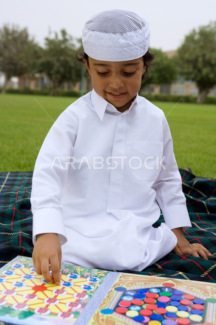 التنزه وقضاء أوقاء صيفية ممتعة ، صورة مقربة لصبي عربي إماراتي خليجي يرتدي الكندورة التقليدية ويلعب ألعاب النرد  , قضاء أوقات ممتعة ومسلية في العطلة, ألعا الذكاء وتنمية المهارات العقلية للطفل ، أماكن سياحية ترفيهية في الخليج العربي.