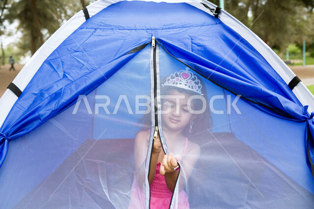 Hiking and spending fun and entertaining times, feeling happy and enjoying summer activities, a close-up picture of an Arab-Emirati Gulf girl sitting inside a small tent, recreational tourist places in the Arabian Gulf