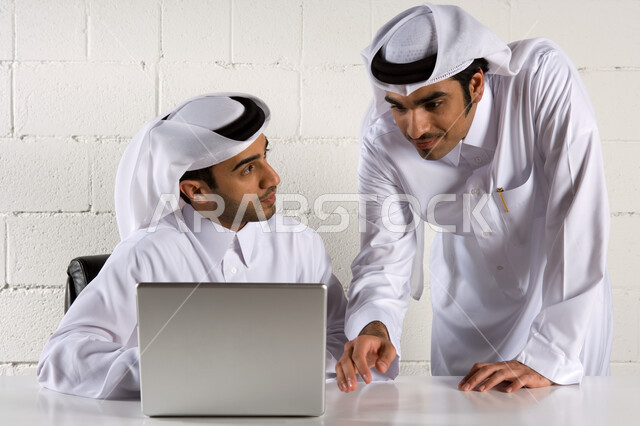 التعاون في تحقيق أهداف الشركة  ،  رجلان أعمال عربيان خليجيان اماراتيان يبتسمان و يرتديان الزي الإماراتي التقليدي ويقومان بدراسة المشروع ،  استخدام الحاسوب المحمول , نقاشات وحوارات حول مخططات العمل ، بيئة العمل في الشركات الإماراتية، خلفية بيضاء