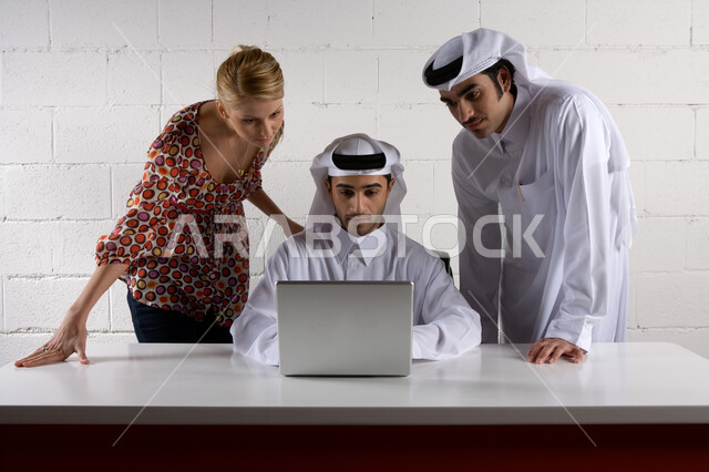  تحقيق أهداف الشركة بالتعاون بين الأعضاء  ،  رجلان أعمال عربيان خليجيان اماراتيان يرتديان الزي الإماراتي التقليدي ويجتمعان مع سيدة أعمال ترتدي الزي الكاجوال ويتناقشون في المشاريع معا  ،  استخدام الحاسوب المحمول , حوارات حول مخططات العمل ، بيئة العمل في الشركات الإماراتية، خلفية بيضاء
