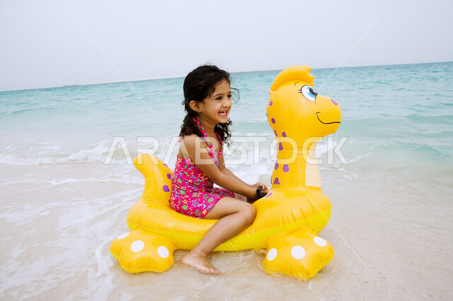 قضاء أوقات مسليه في العطله الصيفيه، ايماءات الفرح والسعاده للقيام بالسباحة، الأنشطة الترفيهية والفعاليات الممتعه، بنت عربية خليجية اماراتية تجلس على عوامه السباحة في شاطئ البحر، زياره المنتجعات والشواطئ الساحلية السياحية في الدول العربيه.