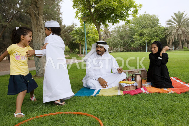 أجواء عائليه مليئه بالحب، قضاء أوقات ترفيهية وأنشطه ممتعه برفقه العائله، أسرة عربيه خليجيه اماراتية تقوم بالجلوس في الحديقة، النزهات والحدائق الترفيهية في الدول العربيه، الاستمتاع في الهواء الطلق، مفهوم الترابط الأسري وحب الأبناء. 