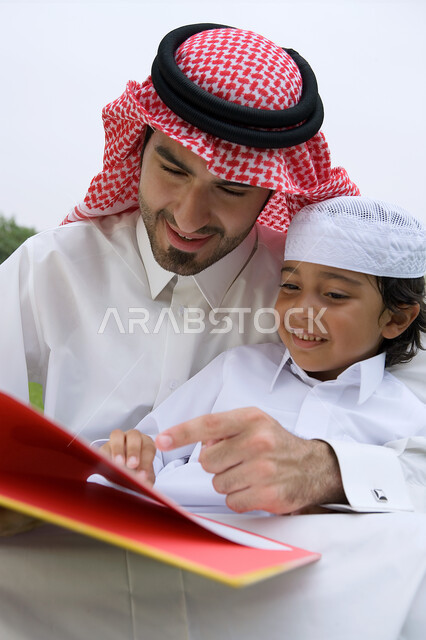  مشاركه الأبناء الأنشطه الترفيهيه المفيده والمسليه، قضاء أوقات ممتعه في إحدى الحدائق في الامارات، أب عربي خليجي إماراتي يرتدي الكندوره والغتره يقوم بقراءه قصة مفيده لابنه،الاستمتاع في أوقات العطله مع أفراد الأسره، منتزهات وأماكن عامه في الدول العربيه.