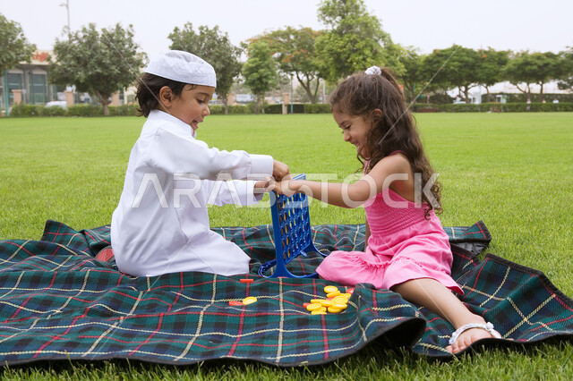 الاستفاده من أوقات الفراغ في اللعب بالألعاب المفيده، تنمية المهارات الفكريه والذهنيه، أخوان عربيان خليجيان اماراتيان يتنافسان للفوز بلعبه اربع تربح، فضاء أوقات ممتعة في الهواء الطلق في إحدى الحدائق العامه في الامارات، ايماءات التركيز والتفكير.