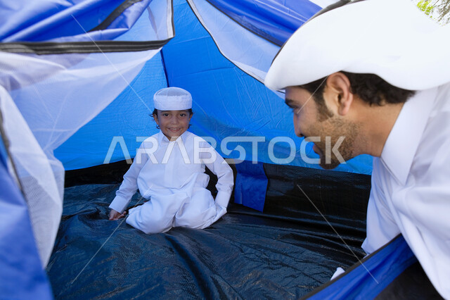 مشاركة الأباء الأبناء أنشطنهم الترفيهية، مفهوم الأبوه والتفاهم مع الأطفال، أب عربي خليجي اماراتي يقوم بقضاء أوقات ممتعه برفقه ابنه داخل خيمه، فعاليات وأجواء تخييم في إحدى الحدائق العامه، الاستمتاع بعطله نهاية الاسبوع مع الأهل.