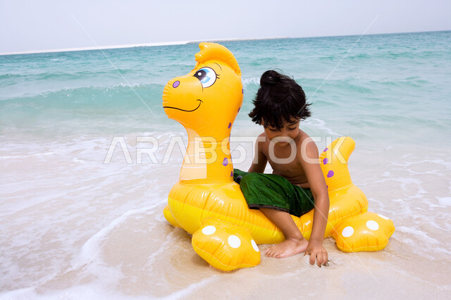 الاستعداد لممارسة هواية السباحه، الاستمتاع والتسليه في أوقات الفراغ، الأنشطة الترفيهية والفعاليات المسليه، ولد عربي خليجي اماراتي يجلس على عوامه السباحة في شاطئ البحر، زياره المنتجعات الساحلية السياحية في دول الخليج العربي، التنزه في الهواء الطلق