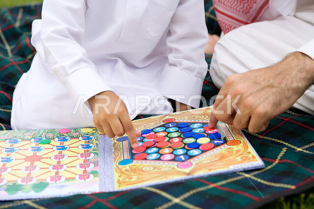 مشاركة الأبناء في الأنشطة الترفيهيه المسليه، صورة مقربة لأب عربي خليجي اماراتي مع ابنه في أحد الحدائق العامة، اللعب بالالعاب الجماعيه, لعبة القتال الورقيه (ذا باتل)، قضاء أوقات ممتعه في الخارج مع الأولاد، الاستمتاع بالعطلة الصيفيه بالتنزه في الهواء الطلق