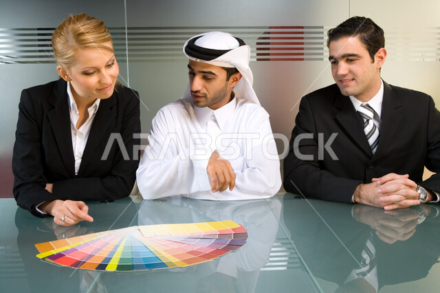 مناقشات وحوارات حول زيادة أرباح الشركة   ، اجتماع عمل بين رجل أعمال إماراتي خليجي  مع موظفين من جنسيات مختلفة  في غرفة الاجتماعات  , الشراكة والتعاون لوضع استراتيجيات معتمدة ,   بيئة العمل في الإمارات  ، خلفية الجدار الزجاجي . 