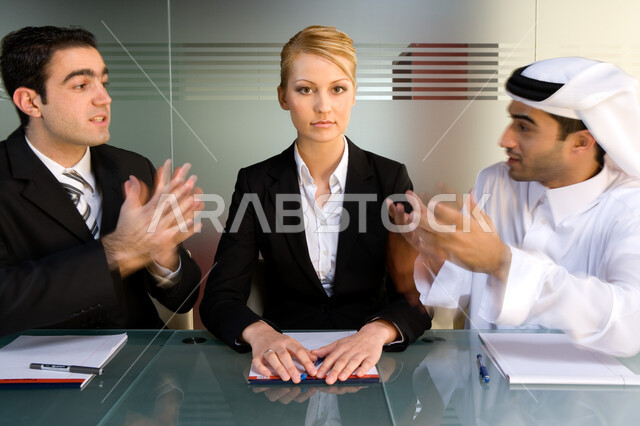 جدالات ونقاشات لحل مشكلات الشركة  ، اجتماع عمل بين رجل أعمال إماراتي خليجي  مع موظفين من جنسيات مختلفة  في غرفة الاجتماعات  , التفاهم و التعاون بين الزملاء لتحقيق الأهداف,   بيئة العمل في الإمارات  ، خلفية الجدار الزجاجي . 