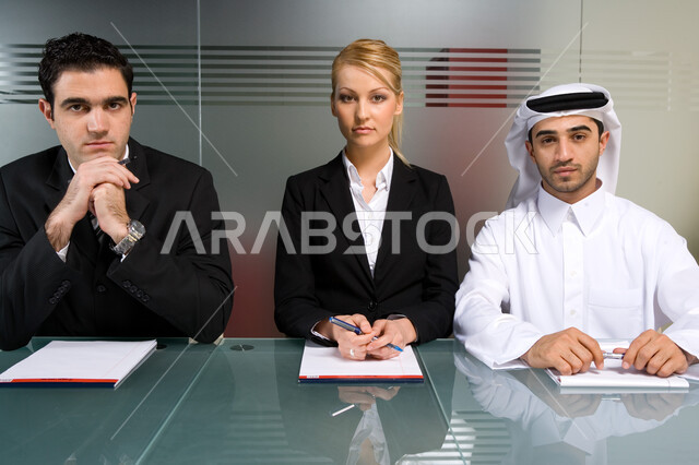 التفاهم و التعاون بين الزملاء لتحقيق الأهداف ,  اجتماع عمل بين سيدة ورجال أعمال من جنسيات مختلفة  ينظرون إلى الكاميرا  داخل مقر الشركة ،  بيئة العمل الإماراتي ،  إيماءات التفكير والتخطيط ، خلفية الجدار الزجاجي . 