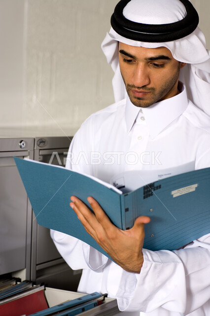 نظرات مليئة بالجد والاجتهاد بالعمل  ، صورة مقربة لشاب عربي إماراتي خليجي يرتدي الغترة و الثوب الإماراتي التقليدي ويبحث في الملفات التعريفية , إنجاز مهام العمل اليومية،  تحقيق أهداف الشركة بكفاءة عالية ، الأناقة والاهتمام بالمظهر الخارجي ،  بيئة العمل الإماراتي . 